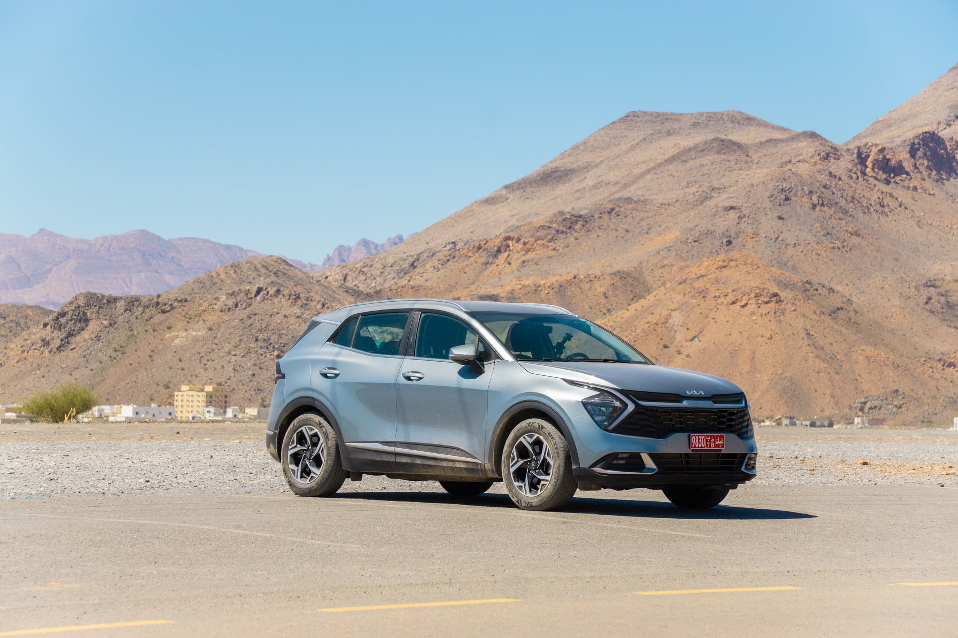 Auto huren in Oman - grijze kia met bergen en blauwe lucht op de achtergrond