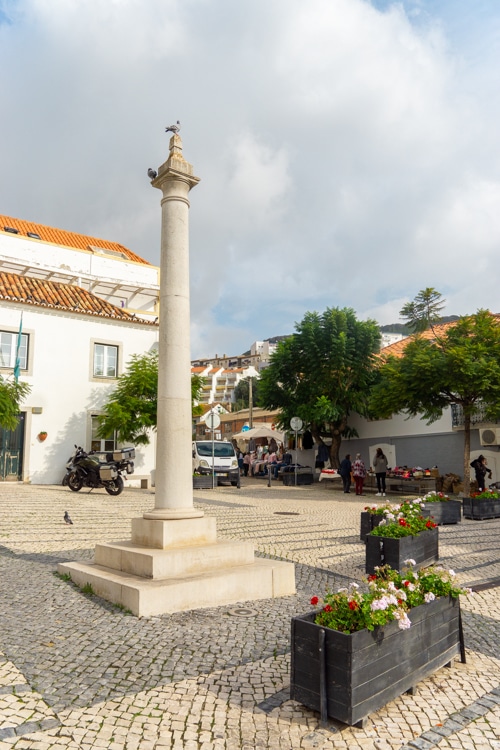 Een plein in Sesimbra, omringd door witte huizen, met een historische pilaar in het midden