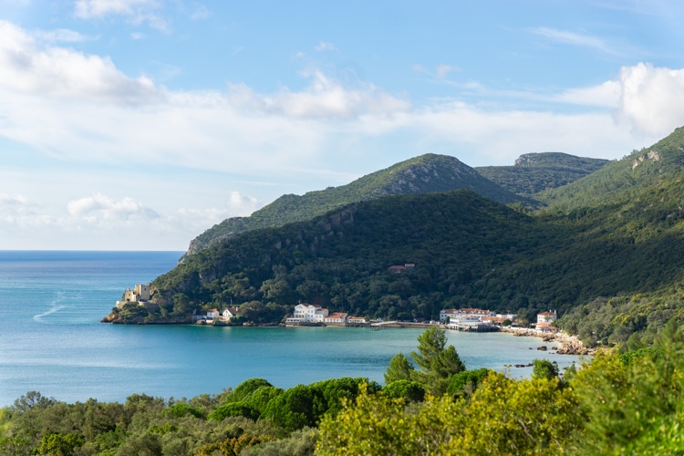 Uitzicht op de schilderachtige baai van Portinho da Arrábida in het natuurpark Serra da Arrábida, Portugal, omgeven door groene heuvels en turquoise water onder een heldere blauwe lucht