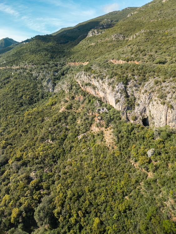 Steile rotswanden en dichtbegroeide groene heuvels in het natuurpark Arrábida bij Sesimbra, Portugal, met een heldere blauwe lucht op de achtergrond.