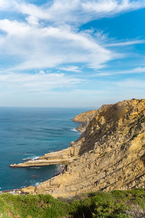 Adembenemend uitzicht op de ruige kliffen van Cabo Espichel in Sesimbra, Portugal, die afdalen naar de blauwe oceaan, onder een heldere hemel met witte wolken