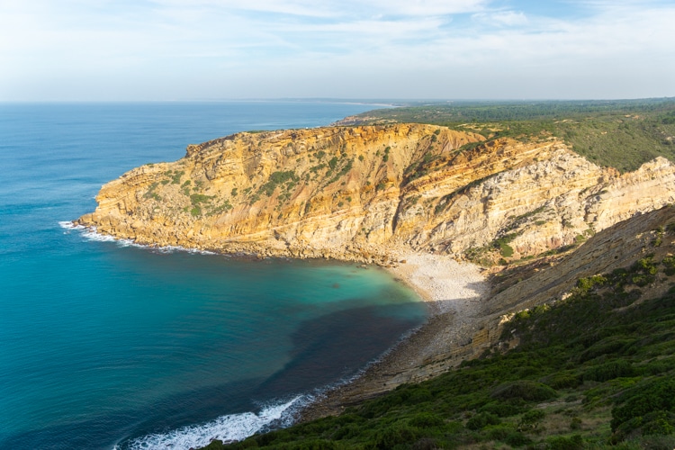 Spectaculair uitzicht op een afgelegen baai bij Cabo Espichel in Sesimbra, Portugal, met steile gouden kliffen, turquoise water en een kiezelstrand.