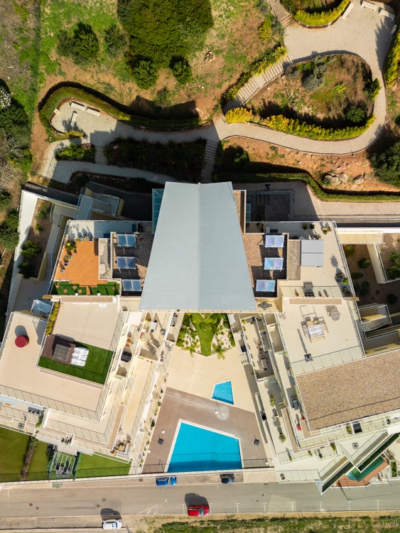 Bovenaanzicht van het appartementencomplex Janelas de Zimbra in Sesimbra, Portugal, met een centraal zwembad en ruime balkons, omgeven door groen en heuvelachtig terrein