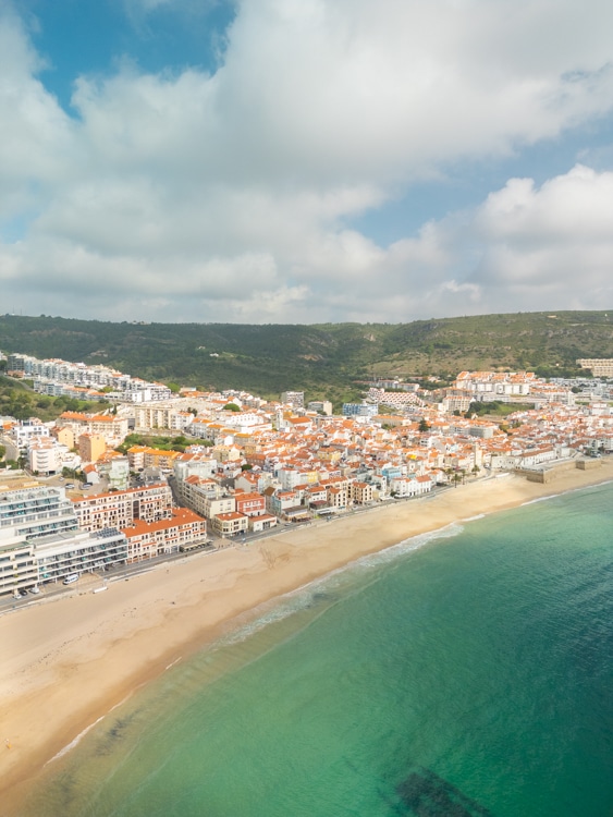 Panoramisch uitzicht op het strand en de stad Sesimbra, Portugal, met witte en oranje gebouwen langs de kustlijn. 