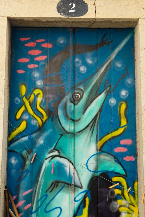 Levendige street art op een deur in Sesimbra, Portugal, met een blauwe zwaardvis afgebeeld tussen kleurrijke zeewieren en luchtbellen