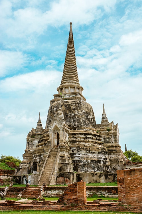 Een historische stoepa in Ayutthaya, Thailand, met verweerde stenen en een indrukwekkend spiraalvormig ontwerp, omlijst door een heldere blauwe lucht. Deze UNESCO-werelderfgoedlocatie is een must-see voor soloreizigers die geïnteresseerd zijn in oude cultuur en architectuur.