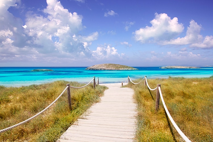 Strandopgang op het zonnige eiland Formentera, blauwe zee en lucht met witte wolken