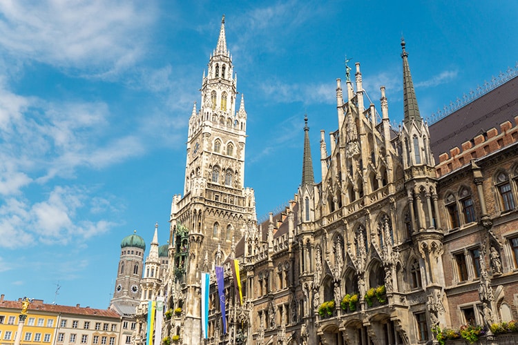 Deze afbeelding toont het Nieuwe Stadhuis (Neues Rathaus) op de Marienplatz in München, een prachtig gotisch gebouw met een indrukwekkende toren en gedetailleerde gevelversieringen. De blauwe lucht en kleurrijke vlaggen geven de scène een levendige uitstraling. Dit is zonder twijfel een leuke plek in Duitsland om te bezoeken, vol historie en charme.