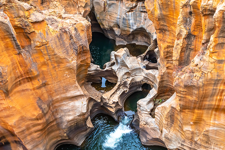 Close-up van Bourke’s Luck Potholes, een spectaculair natuurverschijnsel en een van de hoogtepunten van de Panoramaroute, met cilindervormige rotsformaties uitgesleten door kolkend water tussen roodbruine zandstenen kliffen.