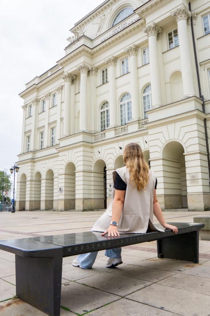 Vrouw zittend op een Chopin Bench voor een statig gebouw in Warschau